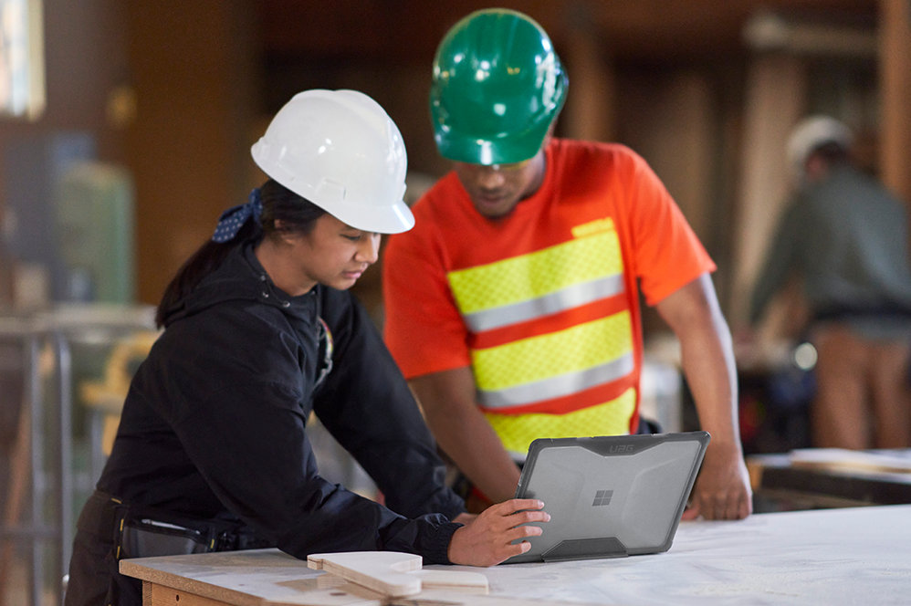 Des personnes portant des casques de sécurité utilisent un Surface Laptop Go 2 pour les entreprises dans un chantier de construction.