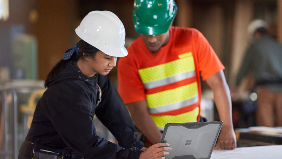 People wearing safety helmets use a Surface Laptop Go 2 for Business from a construction worksite. 