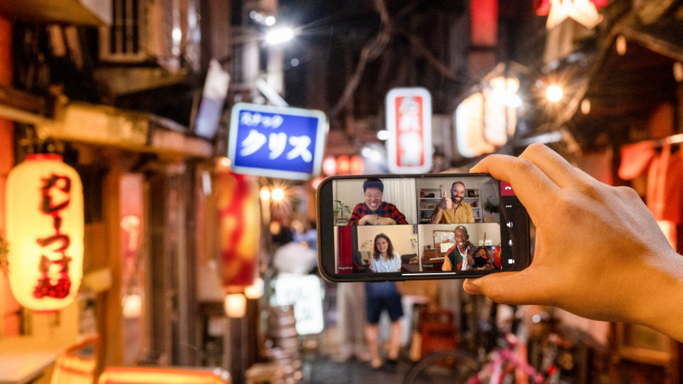 A hand holding up a mobile phone and using the camera to show a Japanese alleyway to a Teams video call. 