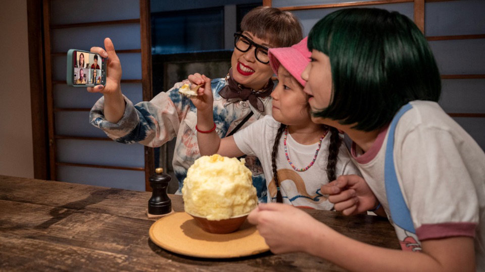 Three people showing off their Kakigōri to a group of people on a Teams video call using a mobile phone.
