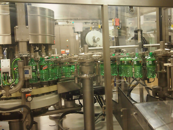 A bottling plant where green bottles are being filled and capped by automated machinery enclosed by transparent safety barriers.