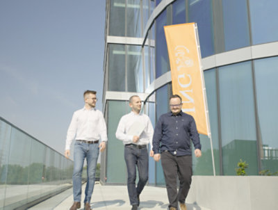 從一棟大樓走出來的三名男性，背景是橙色的 ING 旗幟 