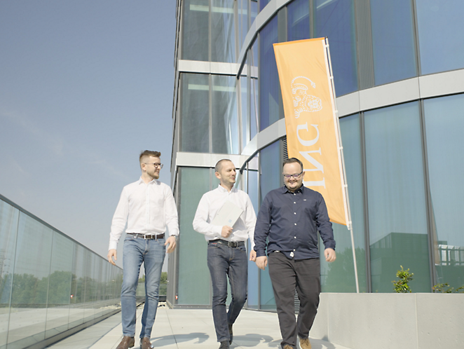 Three men coming out of a buildinng with a Orange ING flag in a background 