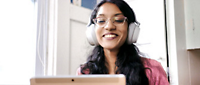 Một người phụ nữ đeo kính và tai nghe đang mỉm cười và sử dụng máy tính xách tay