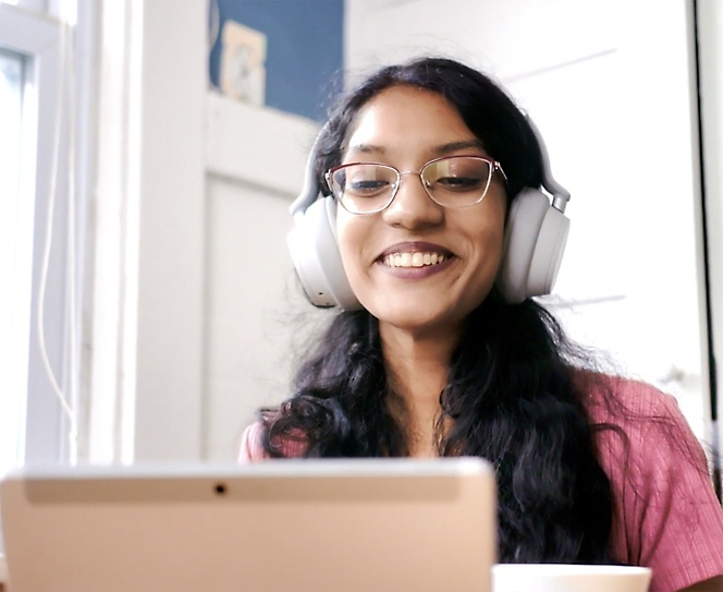 Uma mulher com óculos e auriculares a sorrir e a utilizar o seu portátil