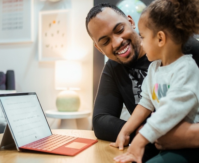 Naeratav inimene vaatamas last, lauale on asetatud sülearvuti