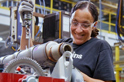 A woman wearing safety goggles working on a machine with visible gears and pipes.