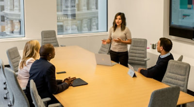 Four people in a conference room seated around a table while one person presents 