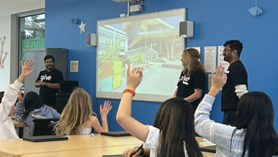 Volunteers in front of a classroom with children seated and listening.
