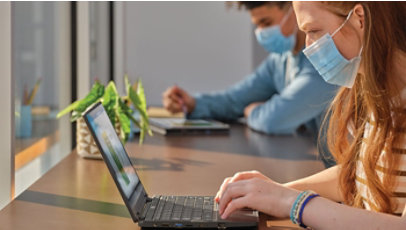 Two people wearing masks sitting next to each other using laptops