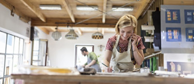 Una donna con il grembiule in piedi in una stanza luminosa con travi di legno sul soffitto. 