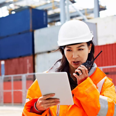 A person wearing a hard hat looking at a tablet and using a walkie talkie