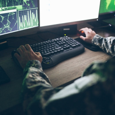 A military personnal typing on keyboard with computer screen infront