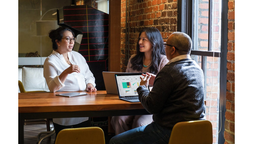 Three business colleagues have a discussion while sitting at a table.