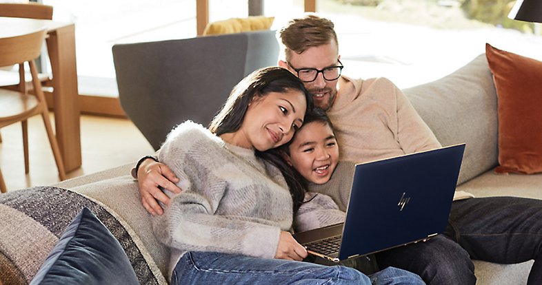 Two adults and a child snuggle on a couch while looking at something on a laptop screen and smiling.