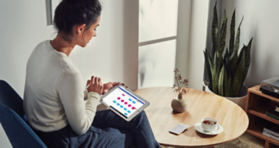 A person sitting at a small round table with a cup of coffee using a tablet device to create a chart.