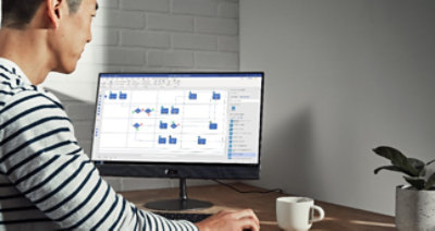 A person sitting at a desk with a plant and a mug working on a desktop monitor.