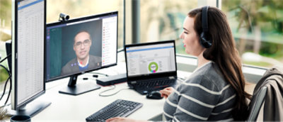 A woman working remotely from home on a multiple monitors, wearing headphones and in a Microsoft Teams video call.