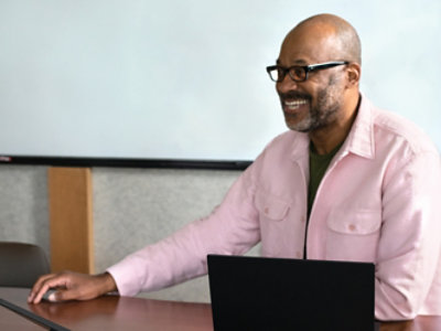 A person sitting at table and smiling while a laptop is open on the table