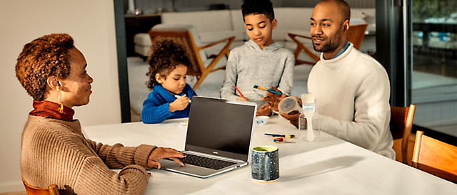 Uma família sentada à mesa com um portátil.