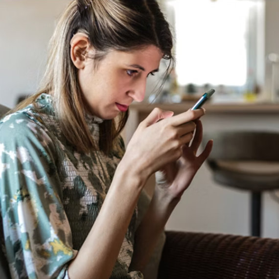 Blind young adult female with hearing aids using a smartphone.