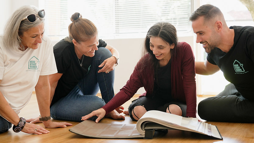 Kamini and her Headstart Homes team sit on the floor of Kamini's new home to look at a wallpaper sample book.
