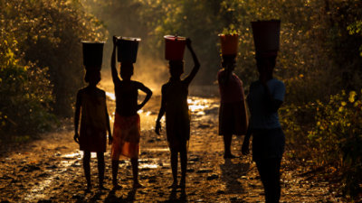 Five women balancing buckets of food and water on their heads.