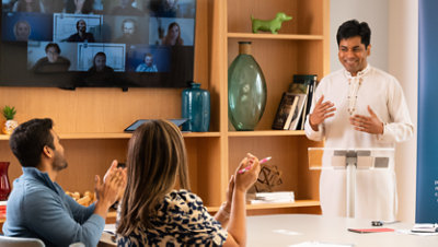 A Toastmaster member presents to a hybrid audience of people in person and in a video call.