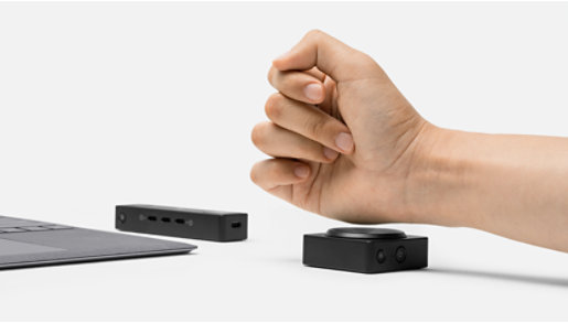 A person's fist hovers over a Microsoft Adaptive Button with Microsoft Adaptive Hub in the background.