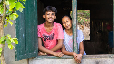 An adolescent boy and a middle aged woman standing together, looking out an open window.
