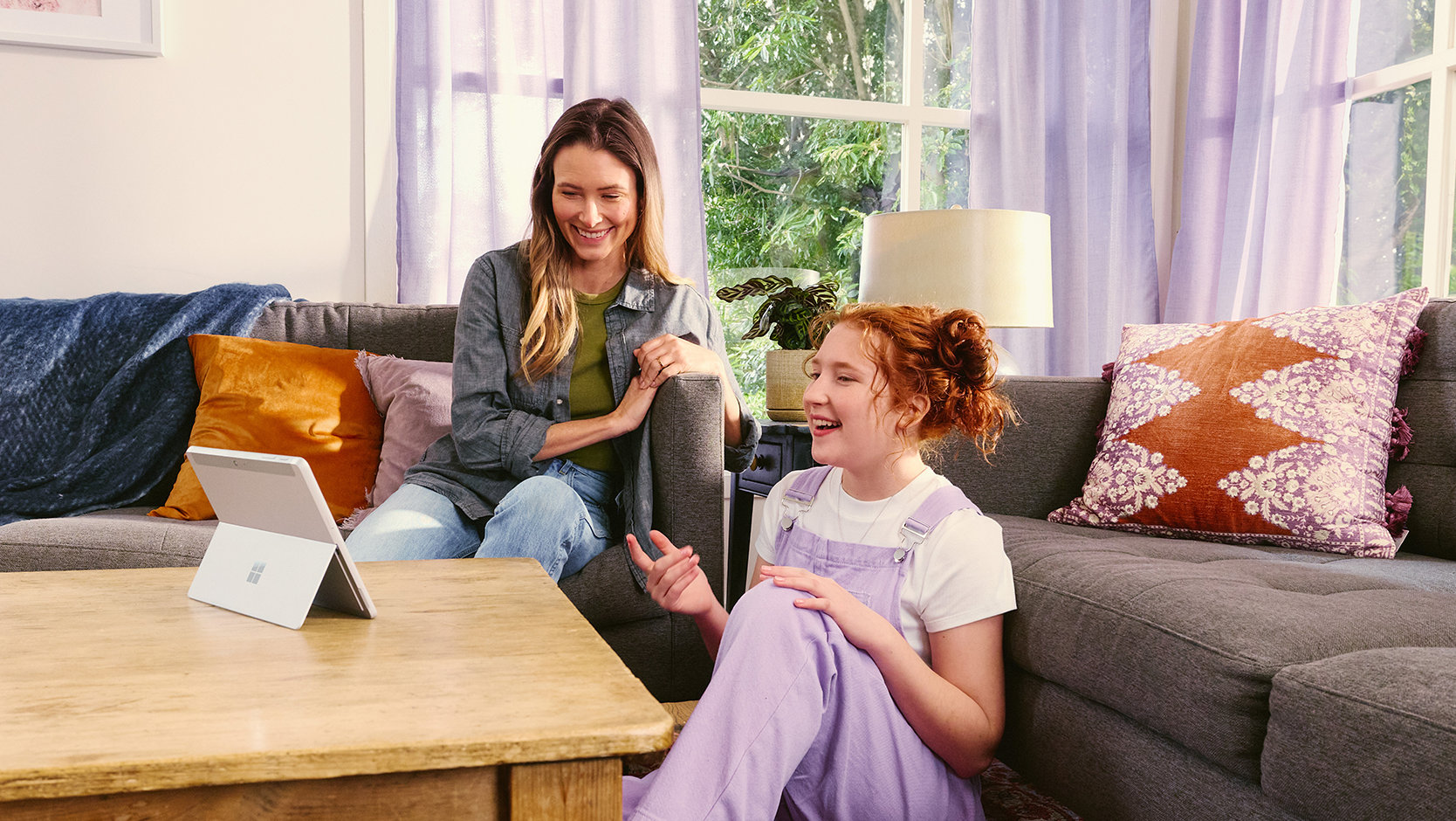 Un adulte et un adolescent sont assis dans un salon et utilisent une tablette ensemble.