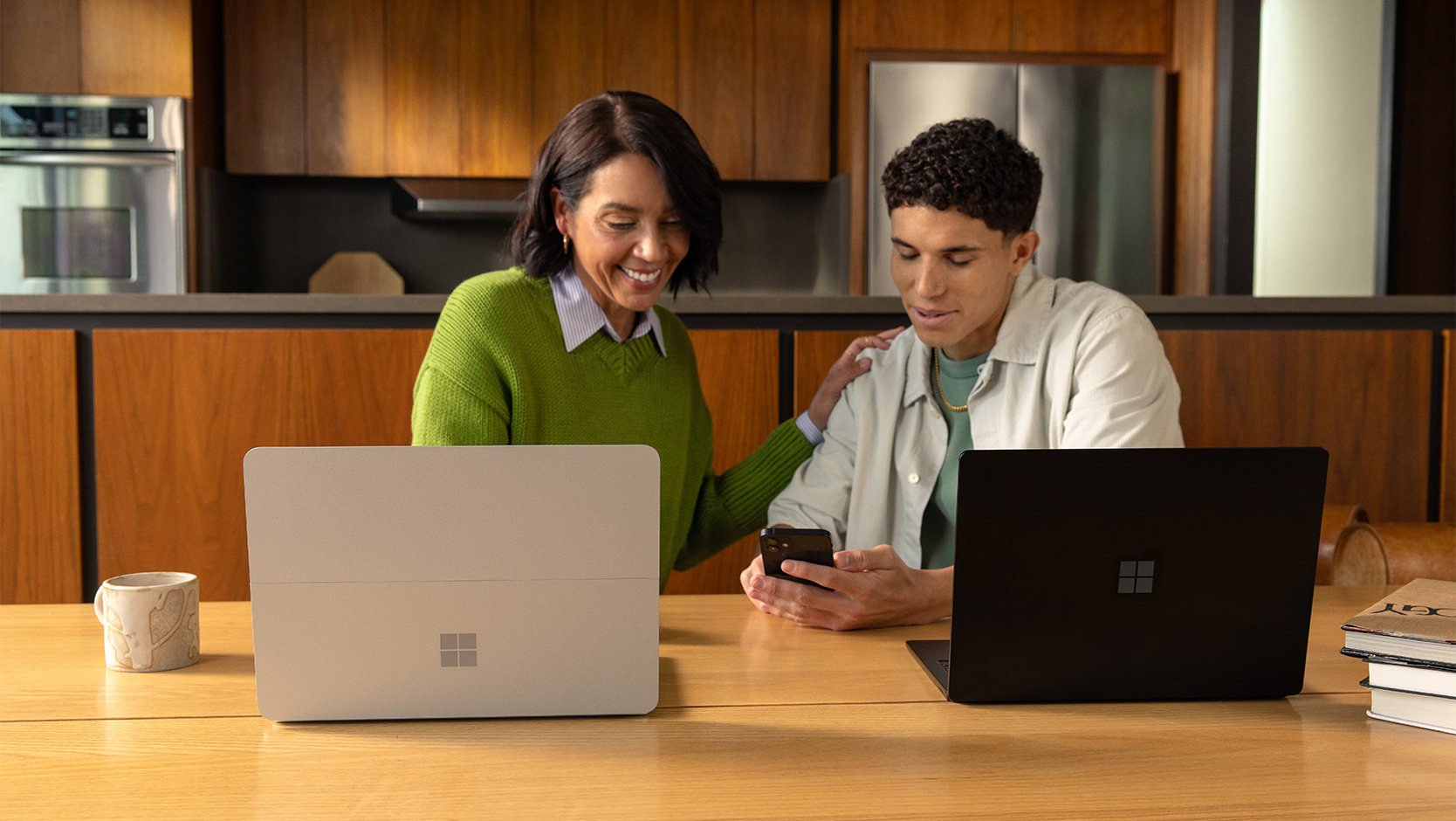 女士與年輕男孩望著手機，桌上放著兩部手提電腦。