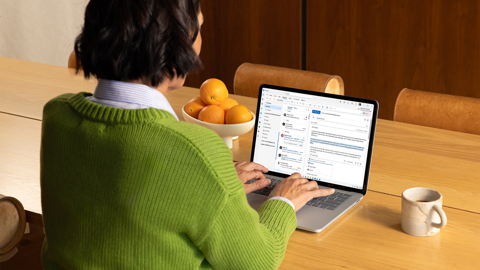 Човек използва Microsoft Outlook на лаптоп, като седи на кухненска маса.