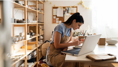 A woman writing in a notebook with a laptop on a desk of a creative studio.