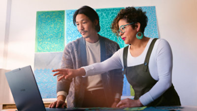 A man and woman in a brightly-decorated conference room work together on a Surface Laptop. 