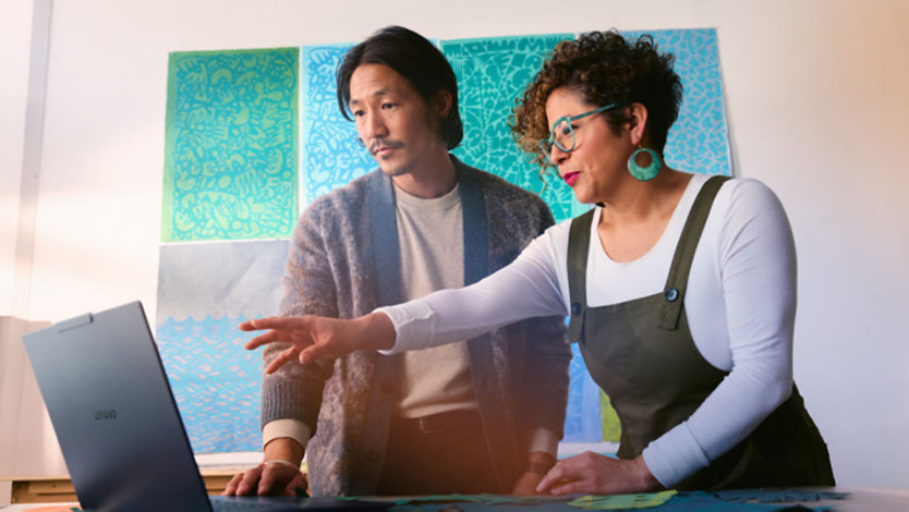 A man and woman in a brightly-decorated conference room work together on a Surface Laptop. 