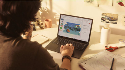 A person using a Surface laptop at a desk filled with notebooks, handwritten notes, and desk accessories.