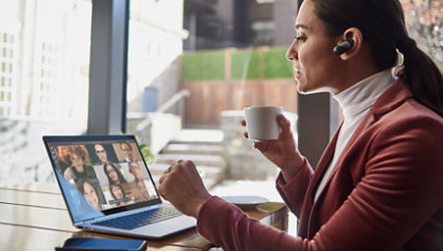 A woman sips a cup of tea and participates in a Microsoft Teams call with her coworkers.