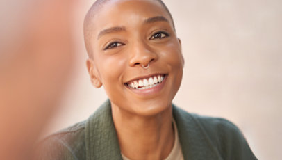 Otuz yaşlarında, siyahi bir kadın gülümsüyor.