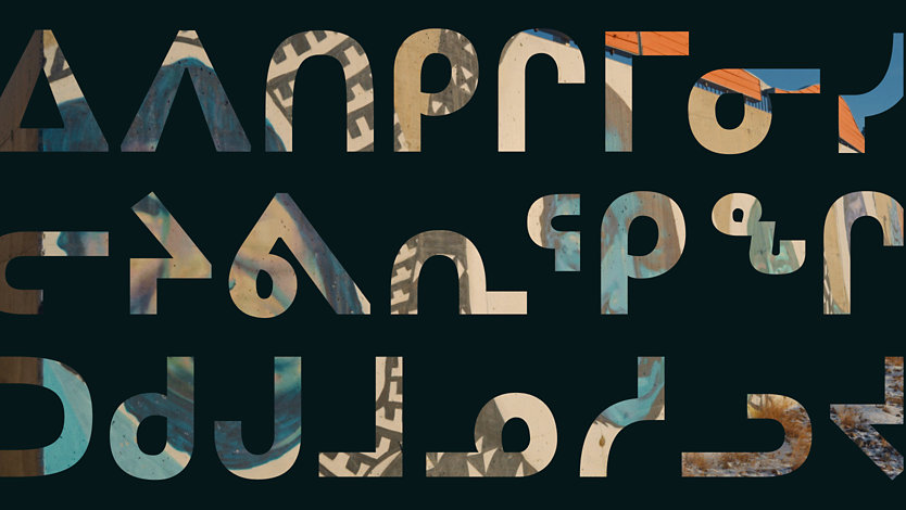 Dark background with large Inuktitut syllabic writing.