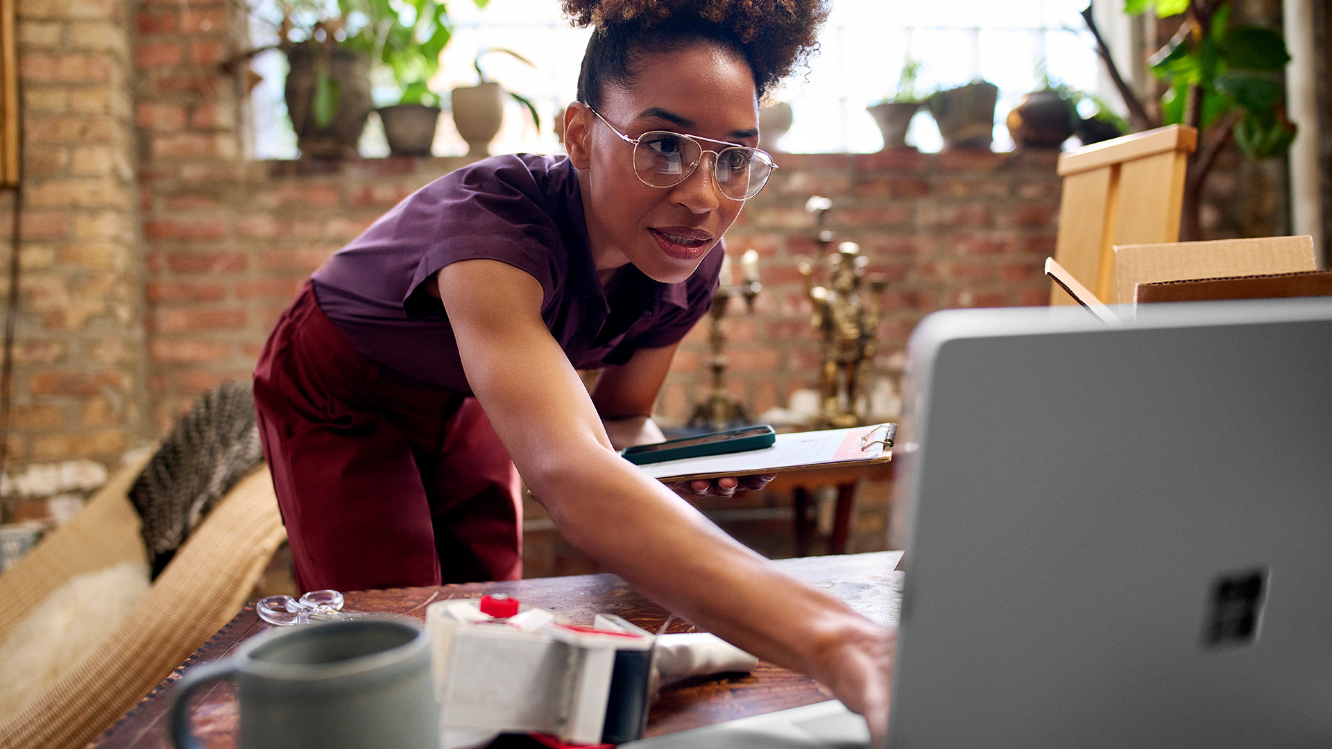 A woman works on a Surface Laptop in a sunny plant-filled room. 