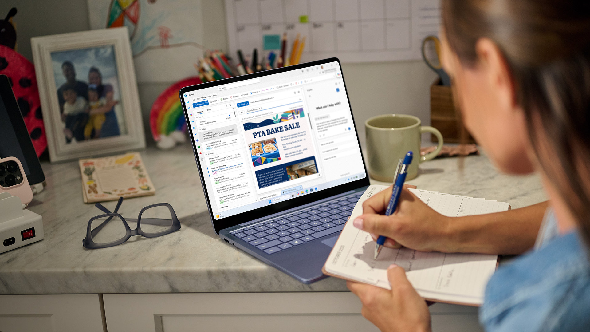 A woman writes in a notebook with a Surface Laptop before her. 