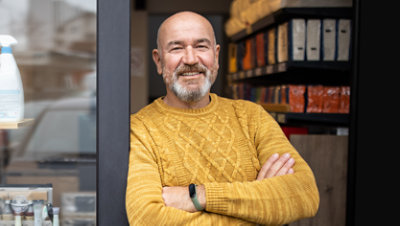Man standing in entryway of his shop, smiling, with his arms folded.