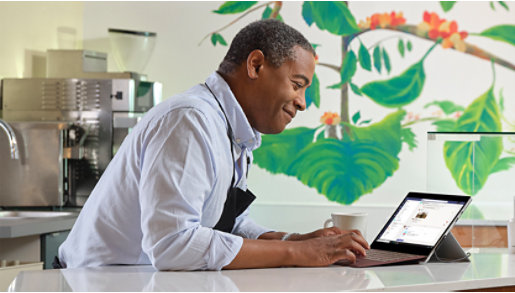 A person behind the counter of a coffee shop, using a Surface device.
