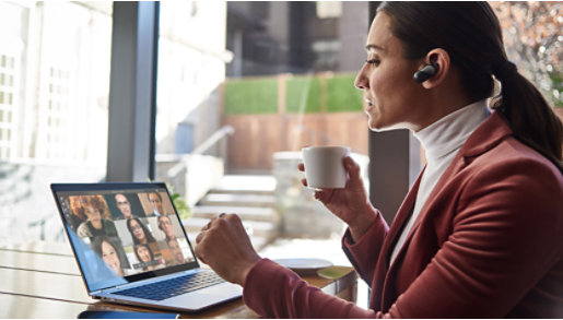 A person wearing aheadset, sitting at a table, drinking coffee, using Teams.