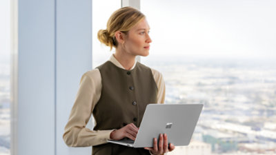 A woman sitting on the edge of a desk holding a Surface Laptop Platinum device. 