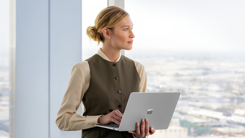 A woman sitting on the edge of a desk holding a Surface Laptop Platinum device.