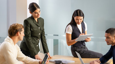 Four people sitting at a conference table, two using Surface Pro 12 inch Platinum devices, and one using a Surface Laptop 13 inch Platinum device. 