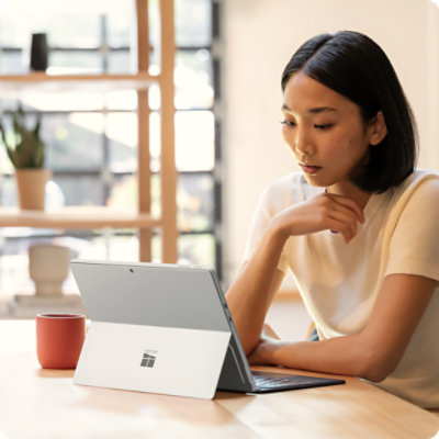 Uma pessoa sentada à mesa, a trabalhar num Surface Pro para Empresas, ligado a um Teclado Flex para Surface Pro de 13 polegadas para Empresas.