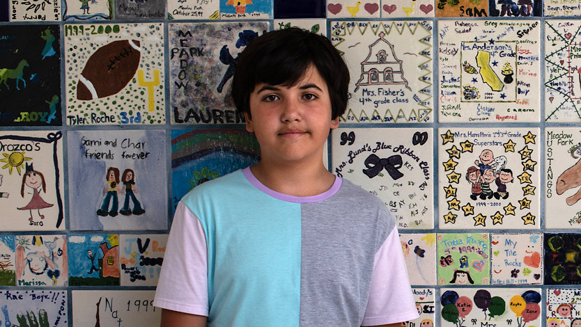 A boy stands in front of a mosaic of student-made tiles.